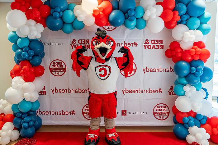 Carthage's Firebird mascot, Ember, poses in front of a wall decorated with Red and Ready decals and balloons.